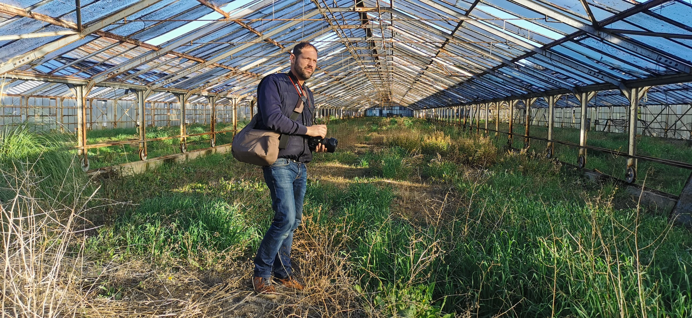 Hugues Bertin, appareil photo en main, dans une serre abandonnée aux parois et à la toiture de verre.